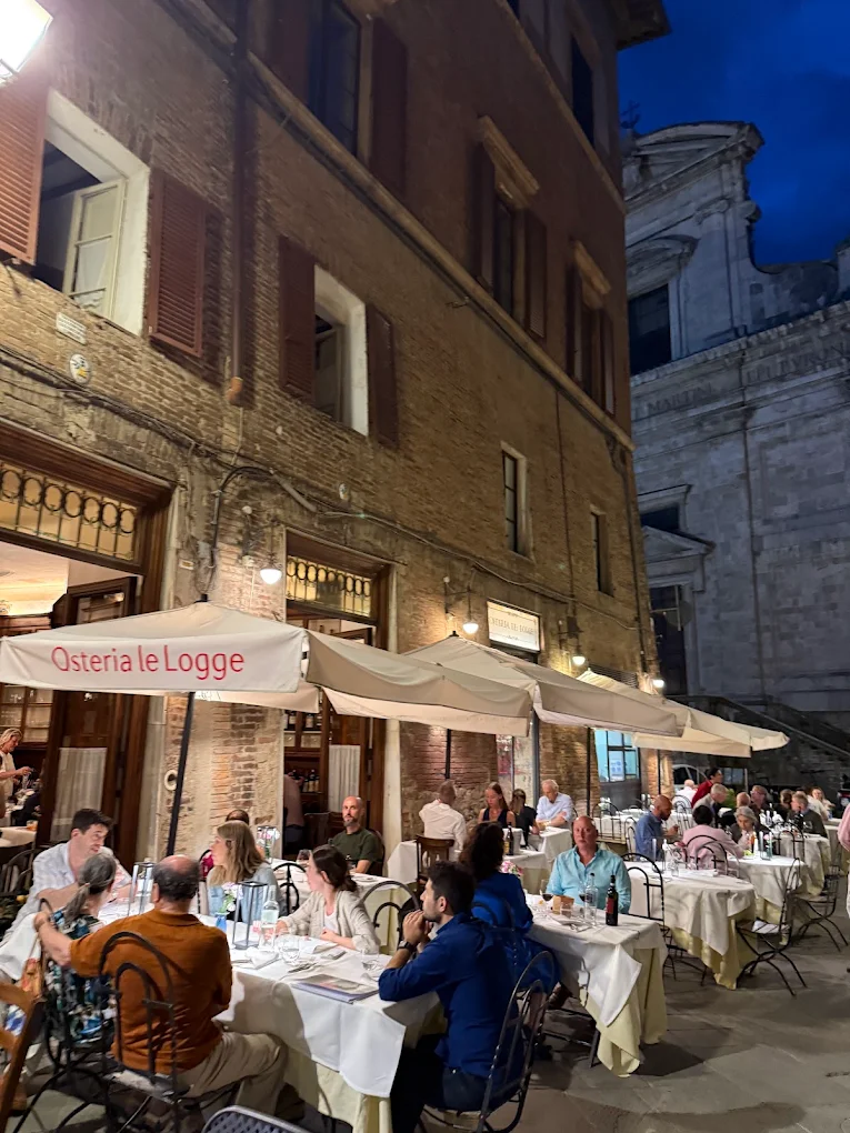 Tavoli all'aperto dell'Osteria Le Logge a Siena di sera con ombrelloni illuminati