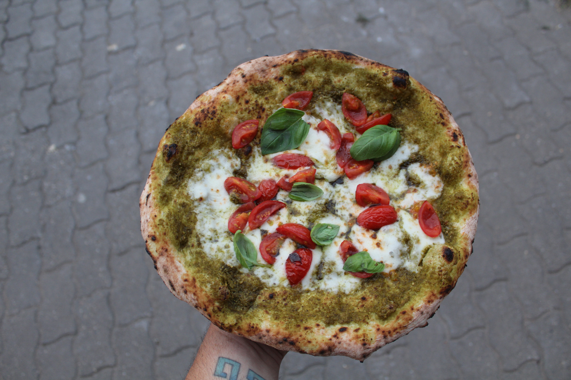 Pizza napoletana con pesto, fiordilatte e pomodorini tenuta in mano