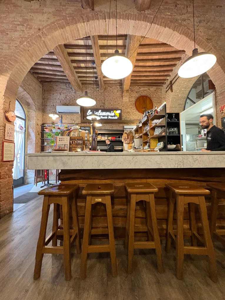 Banco interno Osteria Il Vinaio Siena con arcata in mattoni e sgabelli in legno